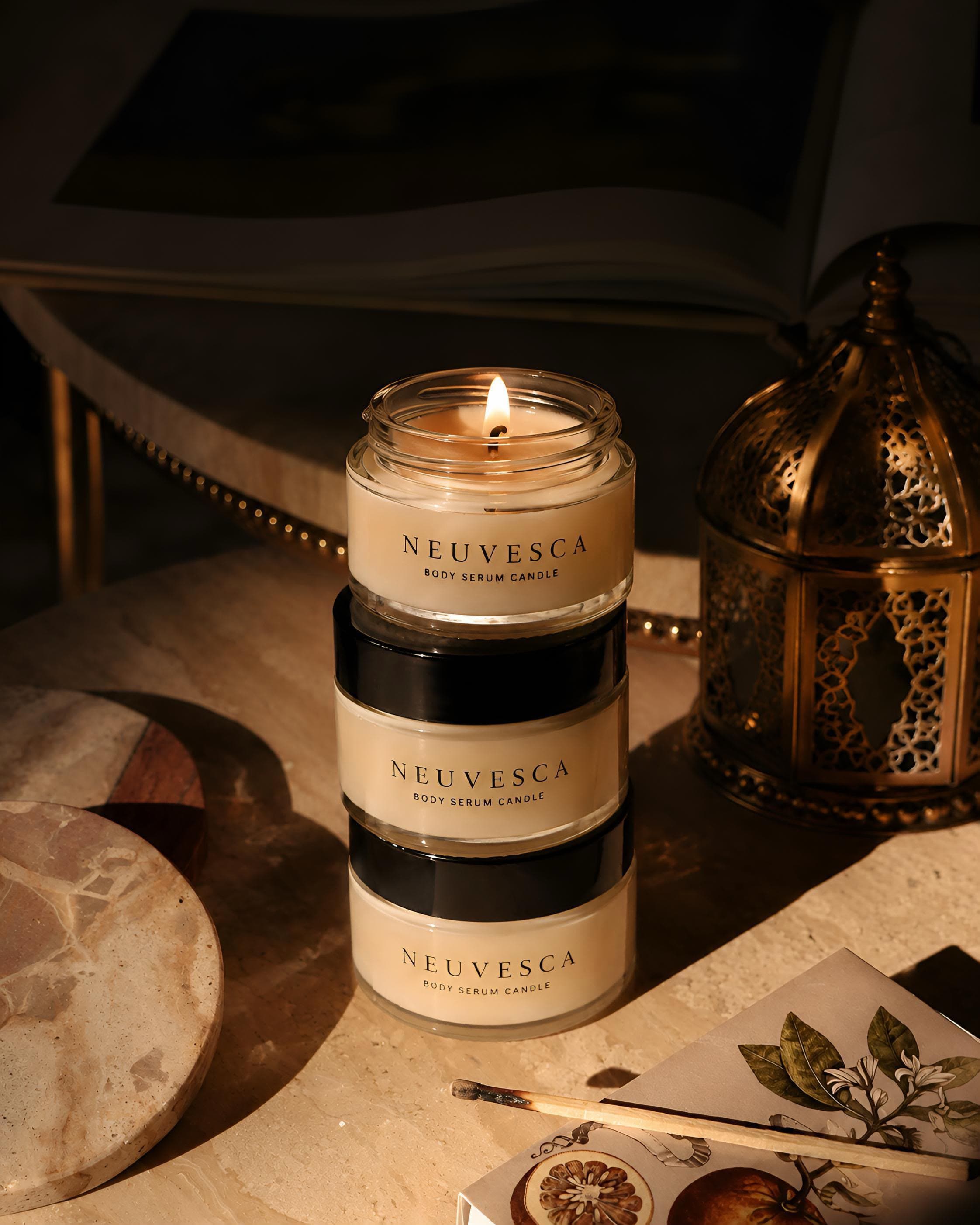 A Neuvesca body serum candle lit beside a brass lantern.